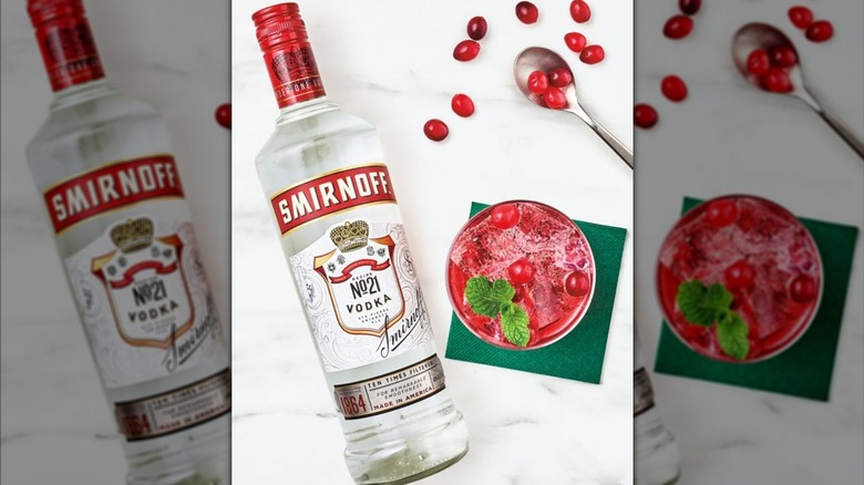 Bottle of Smirnoff vodka laying alongside cranberry drink with spoon and fruit strewn over table.