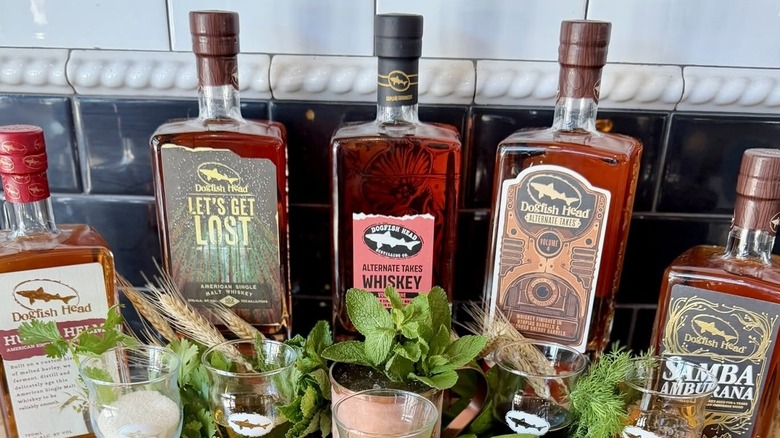 A suite of Dogfish Head spirit bottles on display behind fresh herbs.