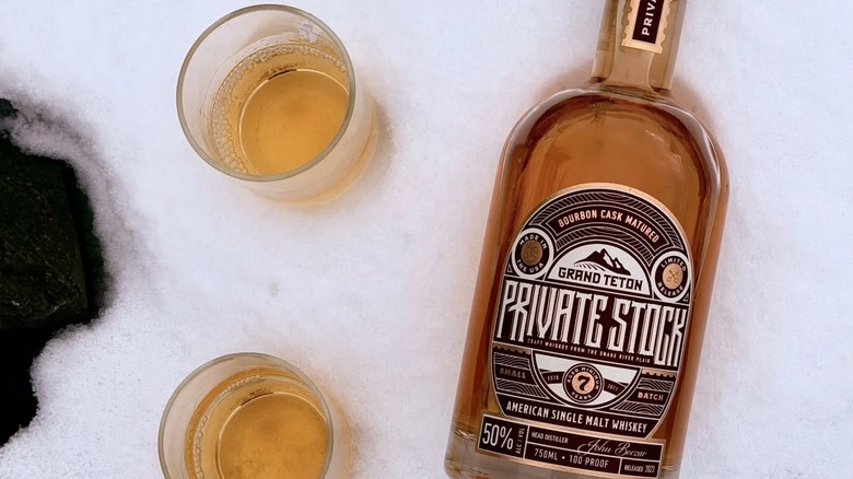 A bottle of Private Stock Whiskey laying in the snow next to two glasses of whiskey.