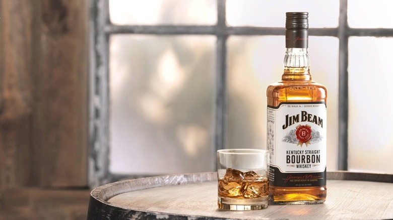 Professional shot of Jim Beam bottle neat to whiskey on the rocks on a whiskey barrel.