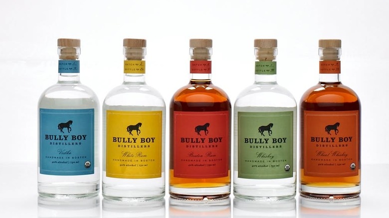 A suite of five Bully Boy bottles of different spirits with colored labels against white background.