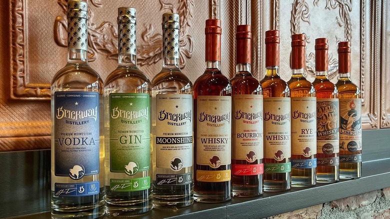 A lineup of Brickway Distillery spirits in tall identical bottles on a mantle in a regal room.
