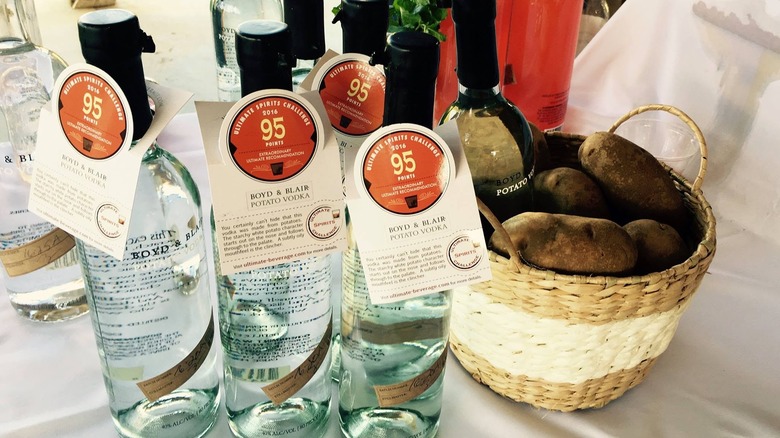 Three bottles of Boyd & Blair Vodka next to a basket of potatoes on an outdoor event table.