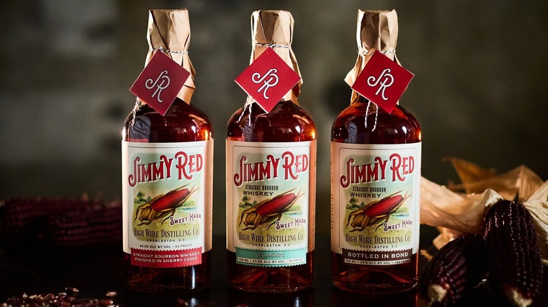 Three nip bottles of Jimmy Red whiskeys alongside dried maize on a dark bartop.