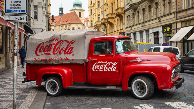 A vintage pickup truck with Coca-Cola branding on the body and the bed covering.