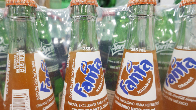 A row of four glass bottles containing orange Fanta.