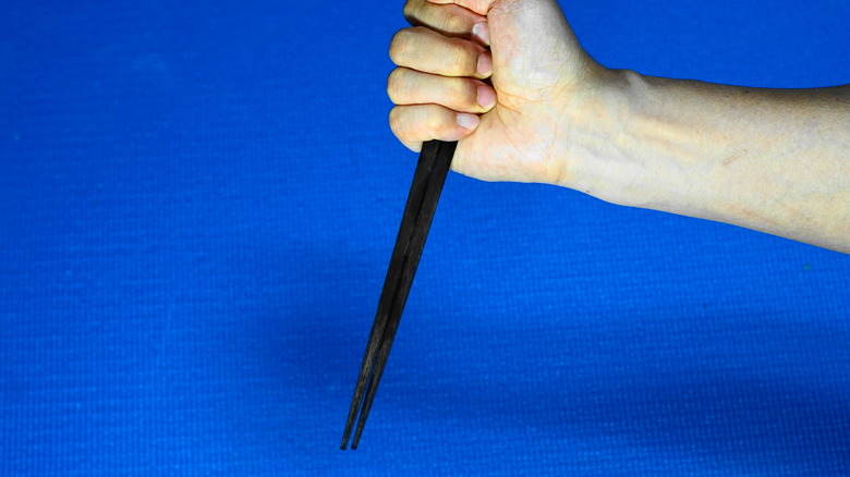A hand holding a pair of chopsticks in a stabbing position