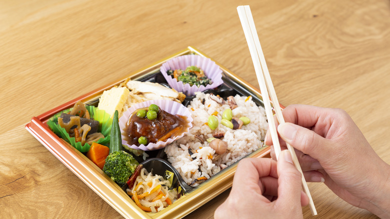 A person breaking apart wooden chopsticks over a dish of Japanese food