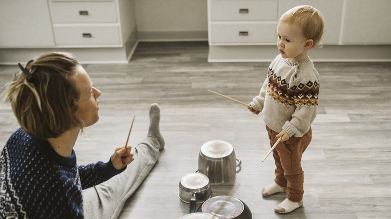 A woman and child playing with chopsticks and upturned saucepans