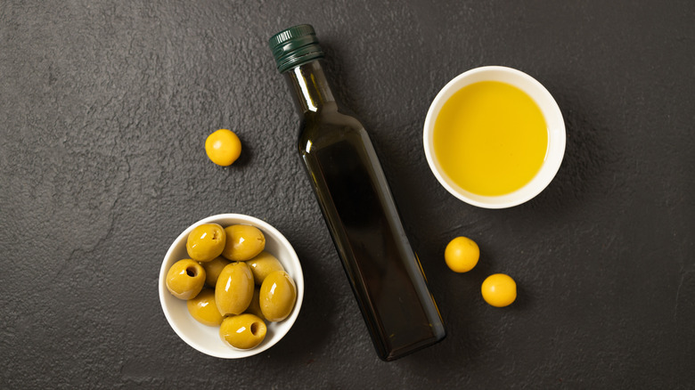 A dark olive oil bottle, flanked by fresh olives and olive oil.