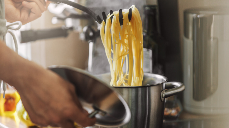 Person stirring spaghetti noodles in a steel pot