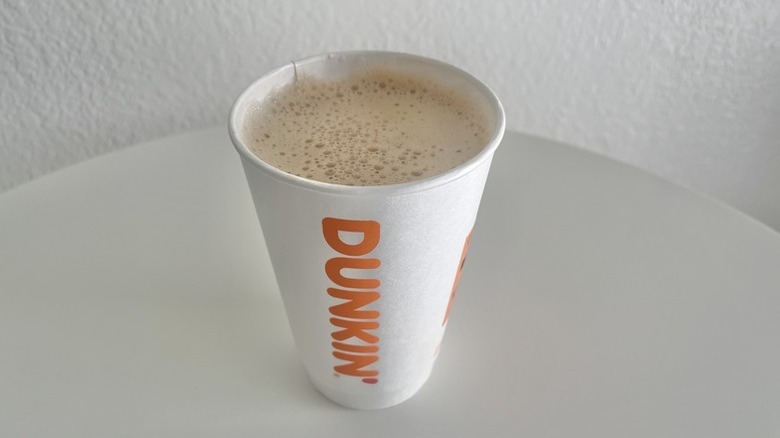 Regular hot macchiato from Dunkin' on a table in a paper Dunkin' cup