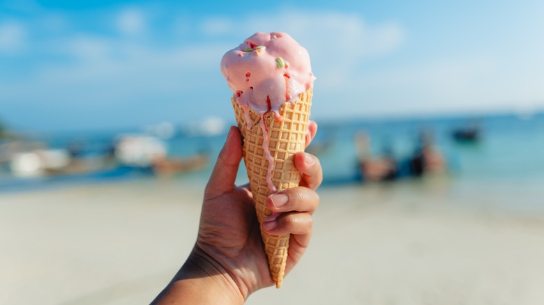 Hand holding ice cream cone at the beach in summer in front of bright blue sky