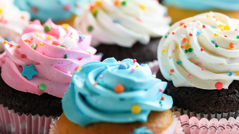 Close up of various cupcakes with pink, white and blue cream with sprinkles