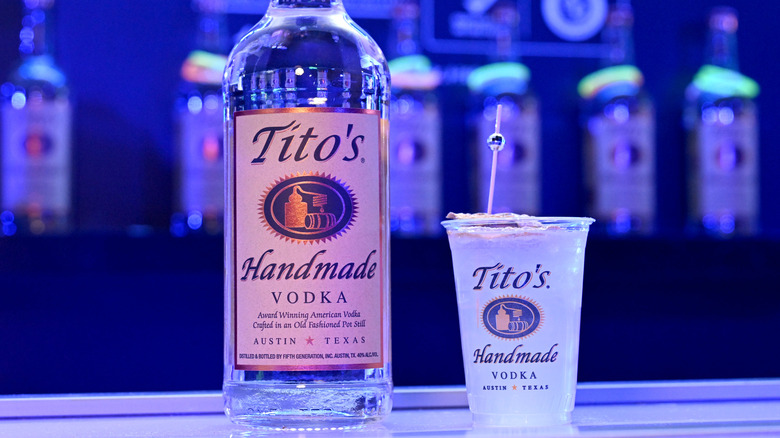 A bottle of Tito's vodka beside a clear cup of Tito's vodka