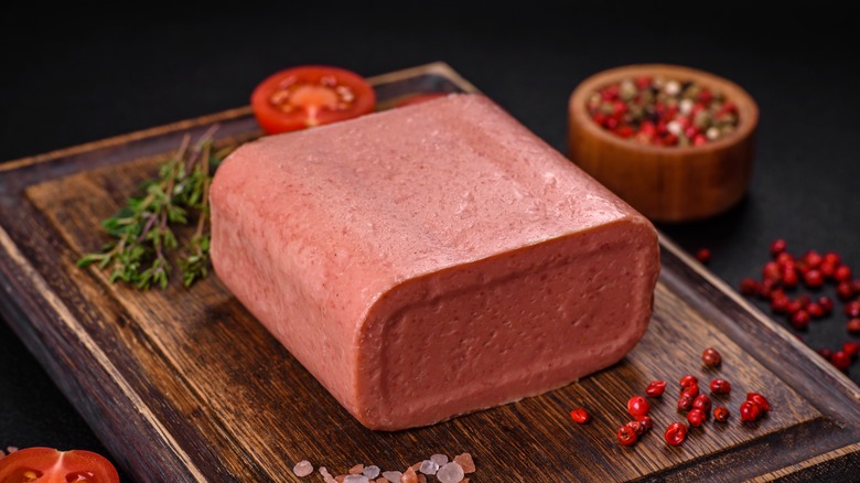 canned pink ham with salt, spices and herbs on a dark concrete background