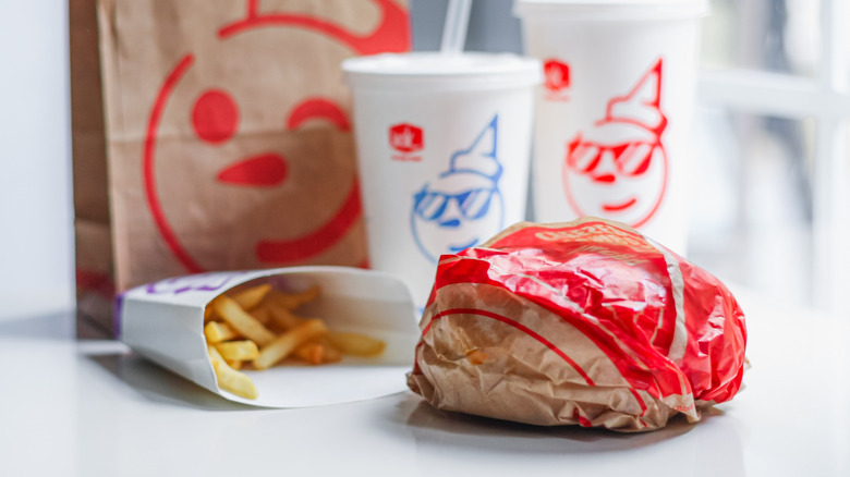 A wrapped Jack in the Box cheeseburger with fries and drinks on a table