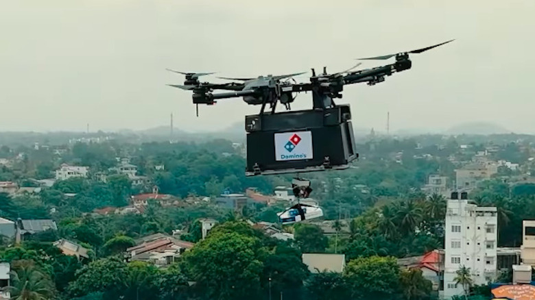 Large black drone with Domino's branding flying in the sky carrying a pizza