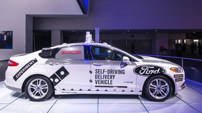 White Ford car with black branding and self-driving delivery vehicle written on the doors
