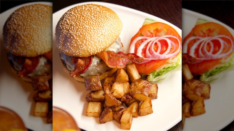 the steak 954 bacon cheeseburger on a white plate, with a side of potatoes