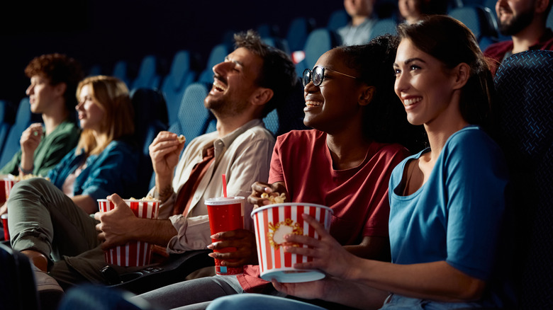 Friends sharing popcorn and laughing at movie theater