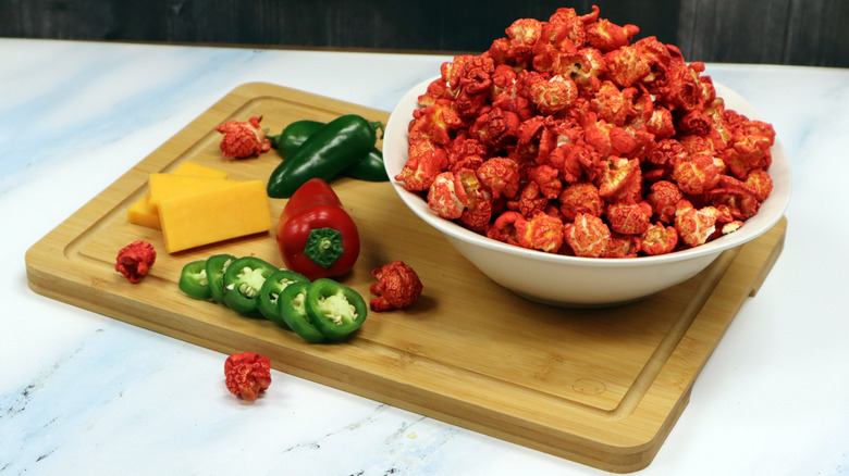 Spicy popcorn on cutting board with peppers