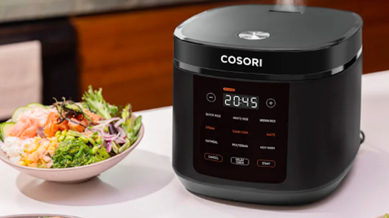 The Cosori rice cooker with steam coming out of the top next to a bowl of vegetables