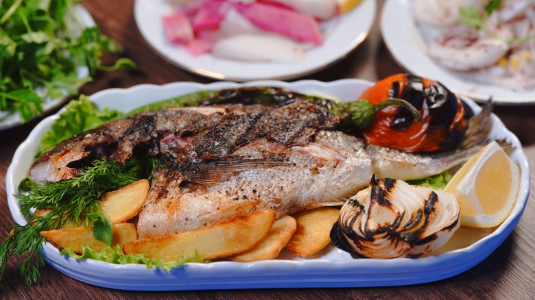 Grilled sea bream with mixed vegetables on a table of other dishes