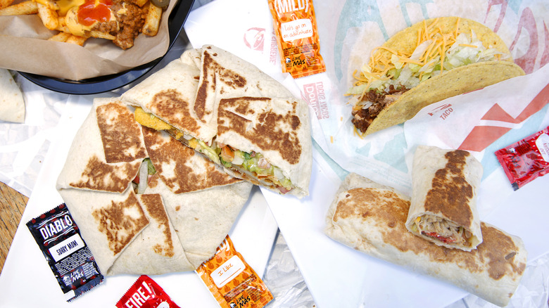 Taco Bell food like the Crunchwrap Supreme and grilled burritos laid out on its wrappers with sauce packets around it
