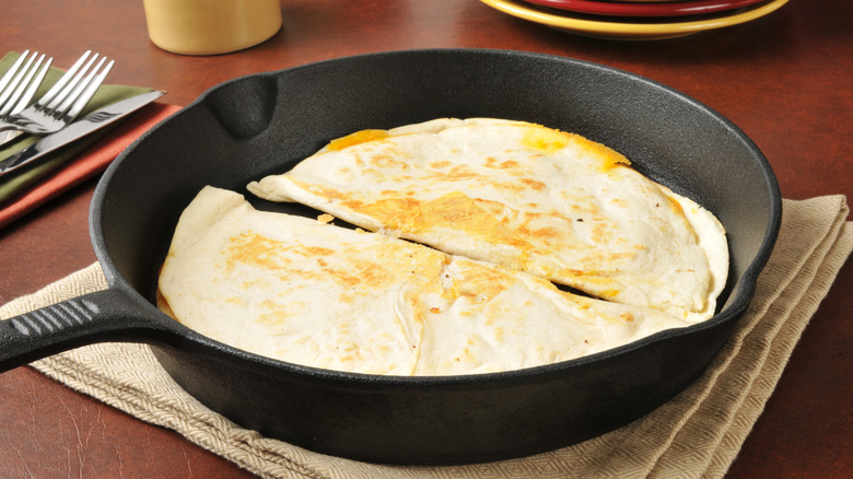 two quesadillas in a cast iron skillet sitting atop a tea towel