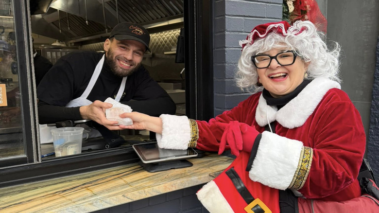 Audrey Giannattasio dressed as Mrs Claus taking food from a server at a window on a Boston Foodie Tour