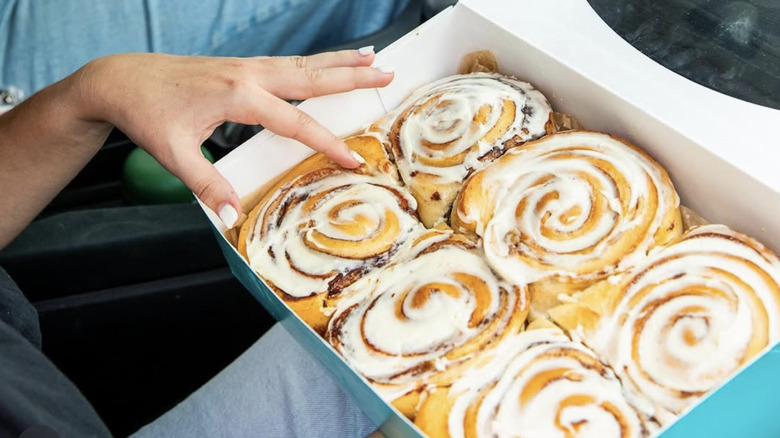 Somone holding box of Cinnabon pastries on lap in car