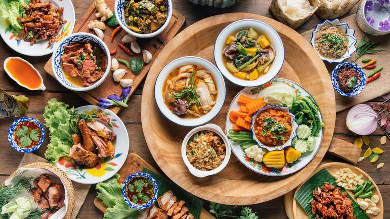a spread of many different Thai dishes in small bowls surrounded by raw ingredients