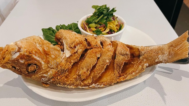 a fried whole red snapper on a plate with mango sauce