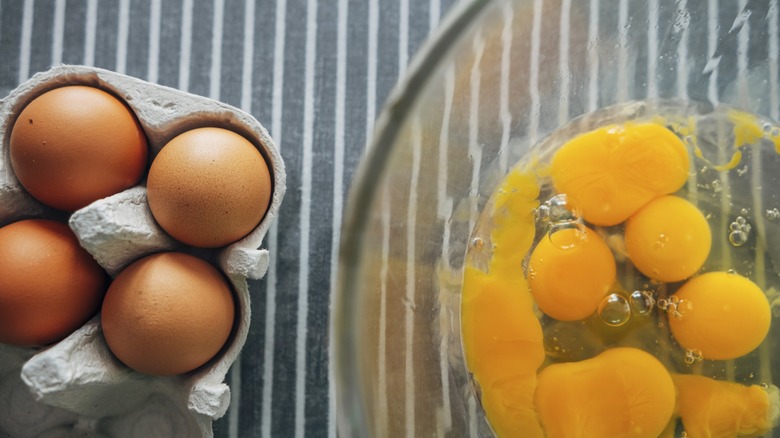 Uncracked eggs in a cartoon next to a bowl of several cracked eggs