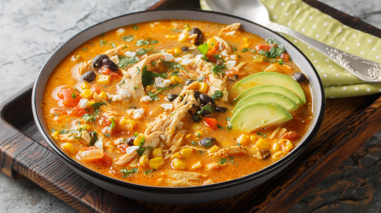 Bowl of black bean soup with shredded chicken and sliced avocado