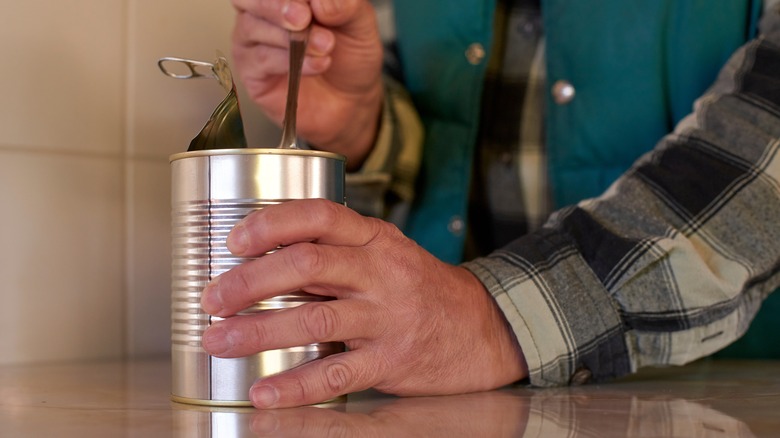 Person opening tin can in kitchen