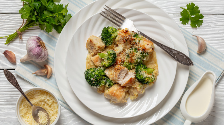 Plated chicken Divan surrounded by fresh herbs, garlic, breadcrumbs, and cream