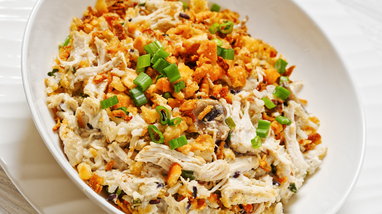 A chicken wild rice casserole topped with fried onions and fresh slices of green onion is served in a white dish