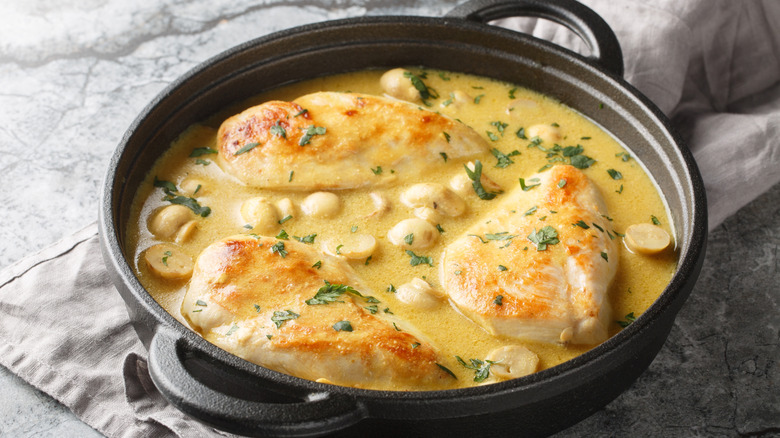 A granite countertop with a dark gray linen napkin is topped with a black cast iron pot filled with a creamy broth, chicken, and mushrooms