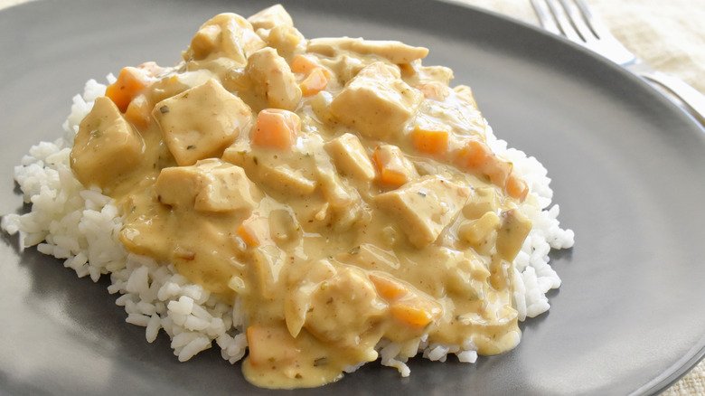 A black circular plate topped with white rice and chicken  à la crème