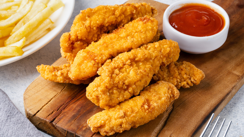Chicken tenders on a tray beside fries and ketchup