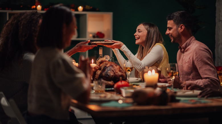 A group passing plates to each other and smiling at a dinner table.