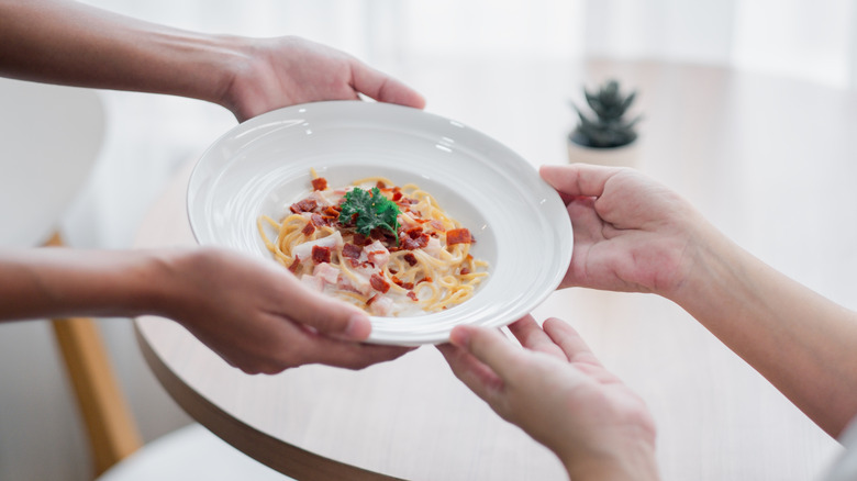 Close-up of hands passing a plate of pasta