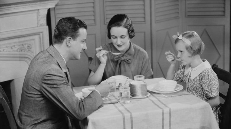vintage photo of mother, father and daughter sitting down to a meal of soup,