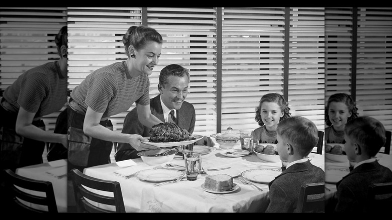 mirrored border woman serving dinner to family around table, black and white vintage image