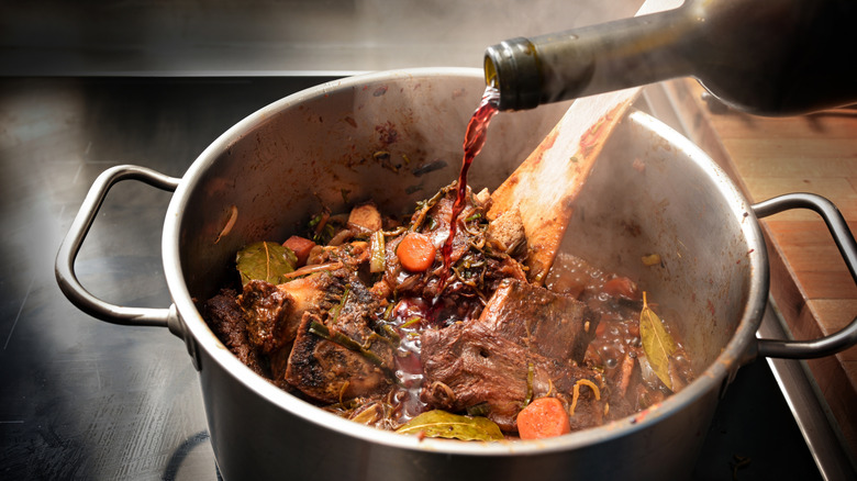 Red wine is poured into a pot of traditional demi-glace ingredients, including meat bones, vegetables, and herbs
