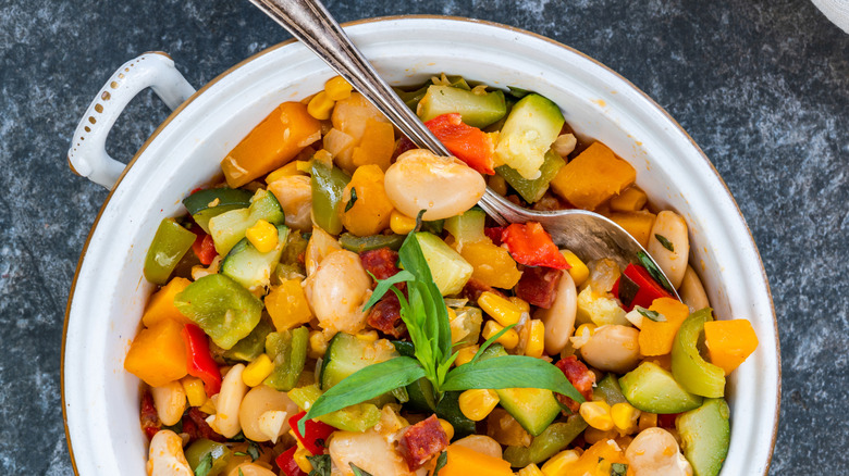 A close up of a pot of succotash with corn, lima beans, onion, bacon, tomatoes, and herbs