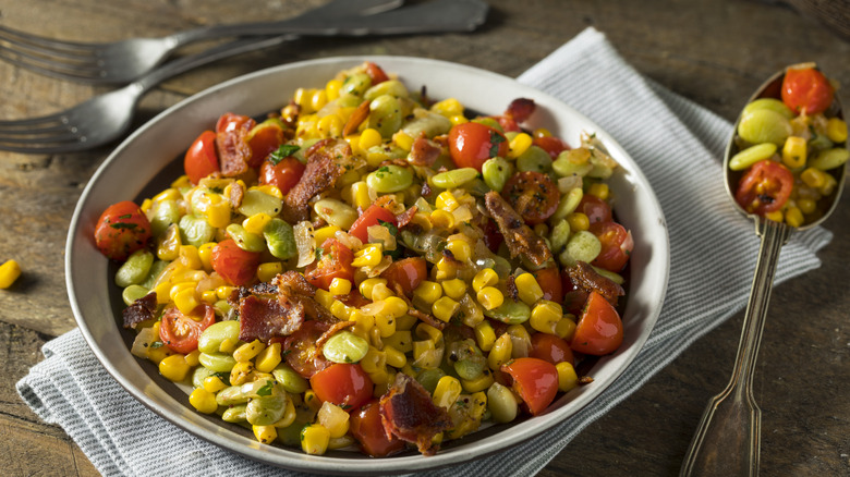 A bowl of colorful succotash with corn, tomatoes, lima beans, and bacon