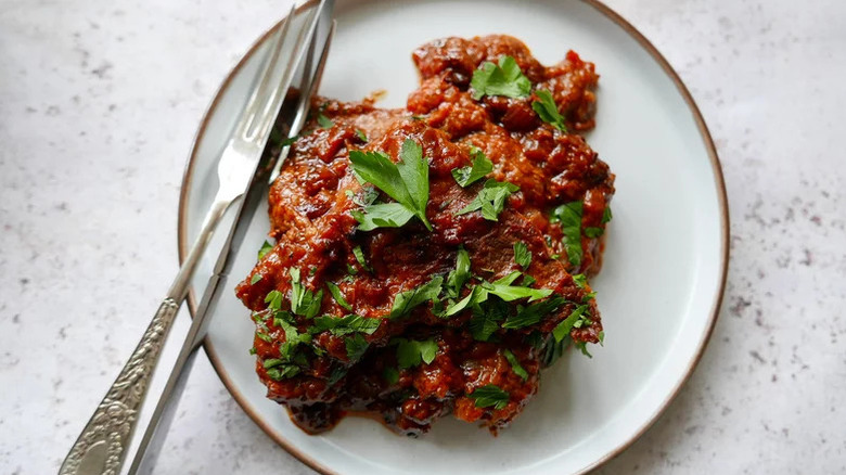 Swiss steak on a white plate, garnished with herbs
